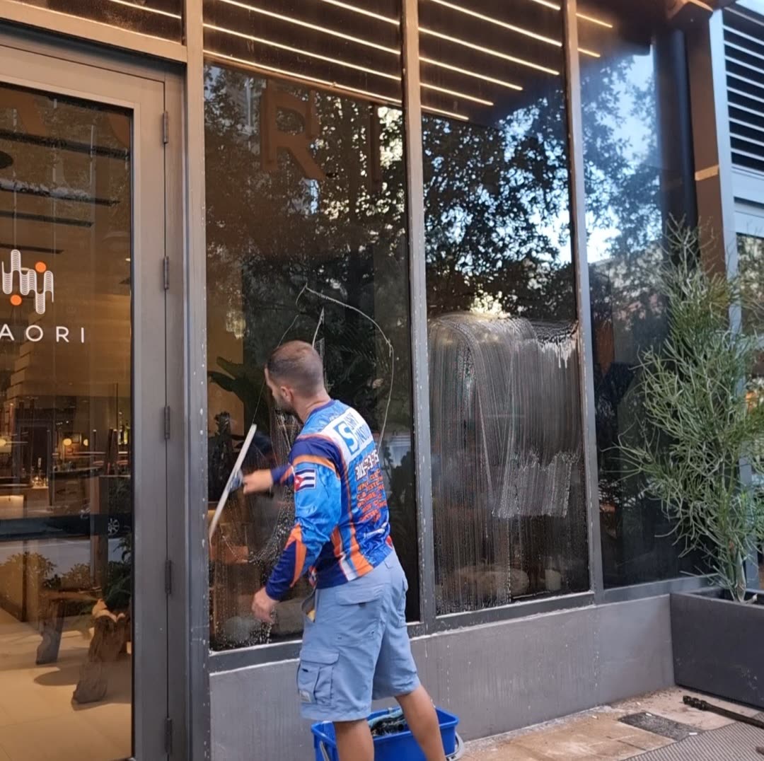 Shiny Windows technician squeegeeing the large exterior glass storefront of Kaori Restaurant in Brickell, Miami, Florida, with soapy water streaming down the freshly scrubbed window