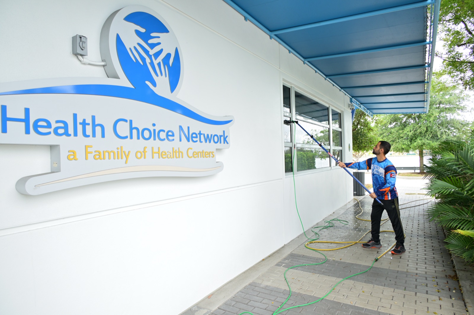 Shiny Windows technician using a water-fed pole to clean exterior storefront glass at the Health Choice Network headquarters in Doral, Florida, the kind of routine professional cleaning that prevents hard water stains from etching the glass