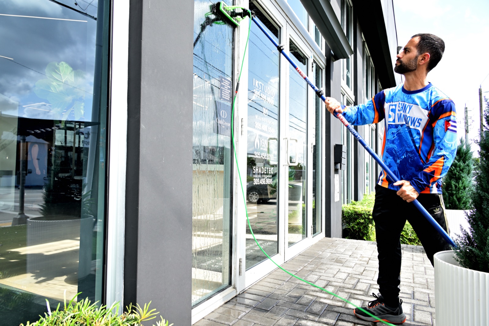 Shiny Windows owner Pedro in branded uniform cleaning storefront glass at IK Studio in Doral, Florida