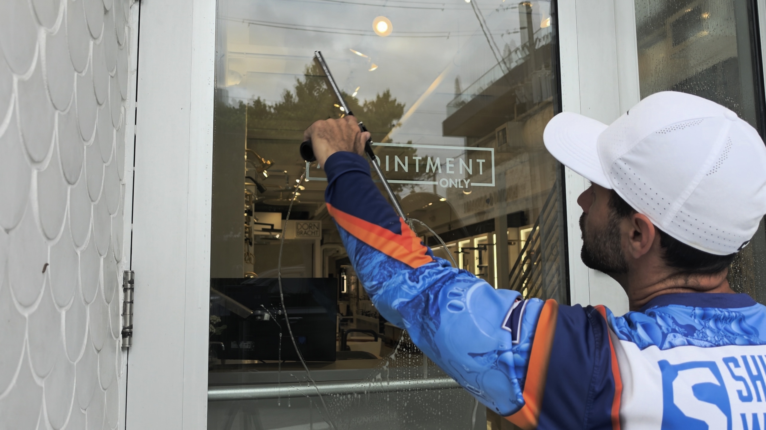 Shiny Windows technician using a rubber squeegee in a fanning motion to leave streak-free, shiny glass on a Miami Design District storefront door