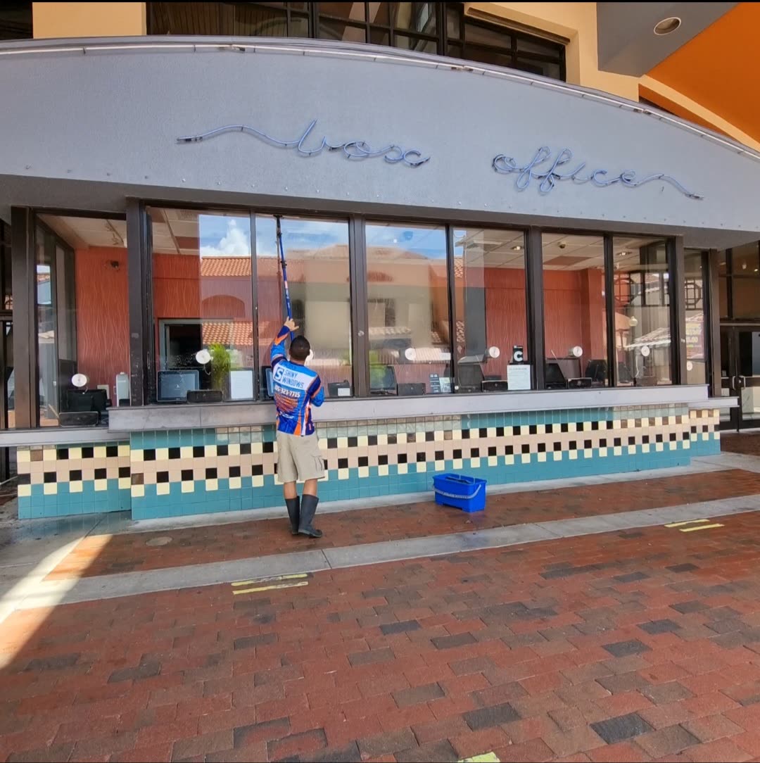 Shiny Windows technician using a water-fed pole to clean the tall exterior storefront glass at the CMX Miami Lakes 13 cinema Box Office entrance in Miami Lakes, Florida, with checkered retro tile work below the window line