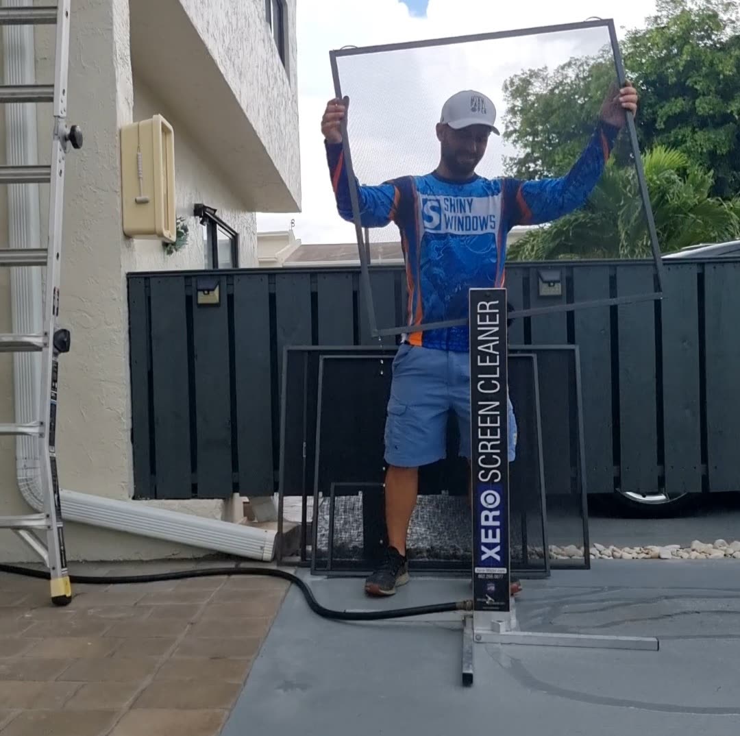 Shiny Windows technician holding up a freshly cleaned window screen next to a Xero Screen Cleaner machine, after completing an exterior window and screen cleaning job at a home in Miami, Florida