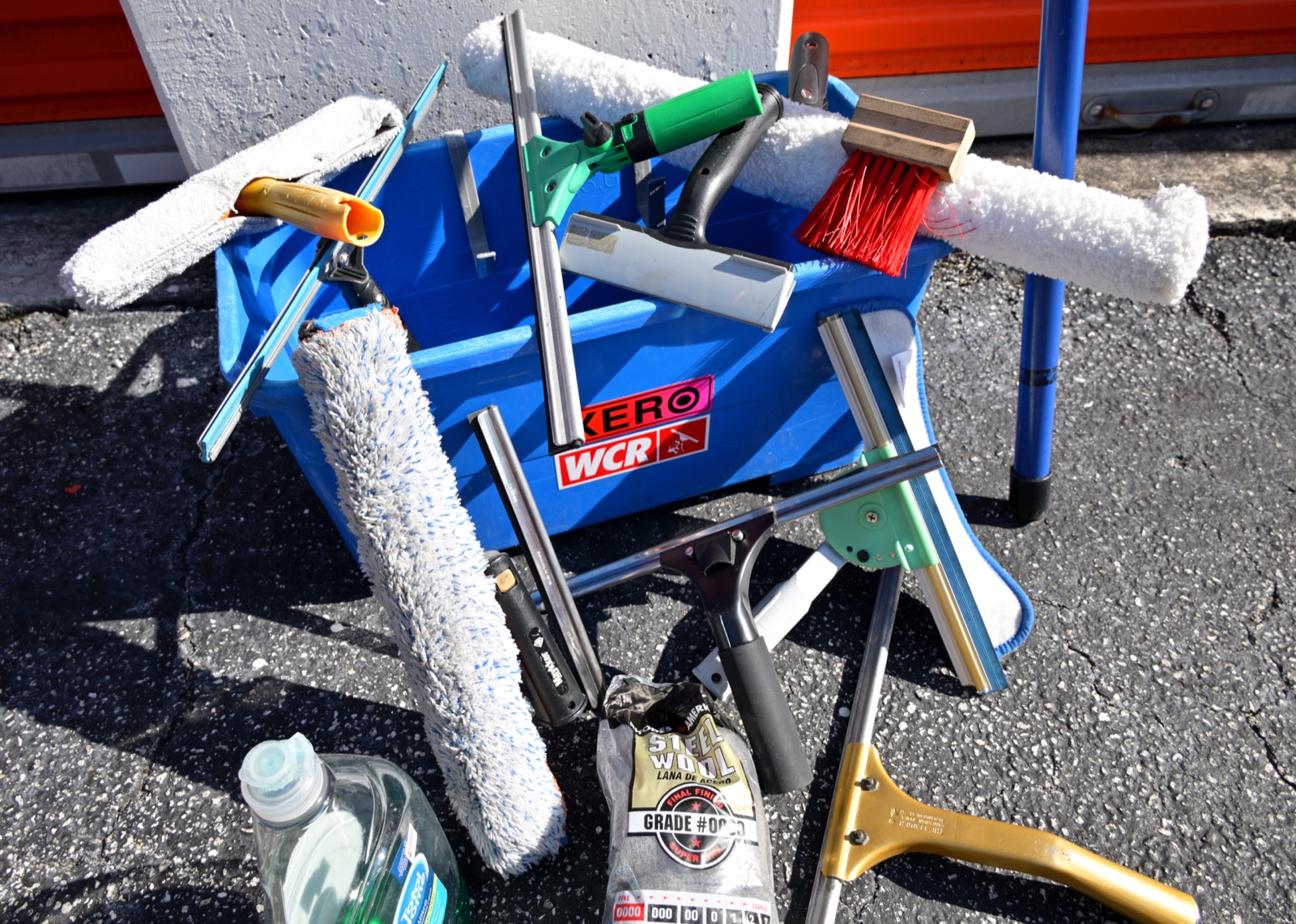 Shiny Windows traditional window cleaning kit: brass squeegees, T-bar microfiber scrubbers, steel wool, and mineral remover laid out in a WCR Xero bucket