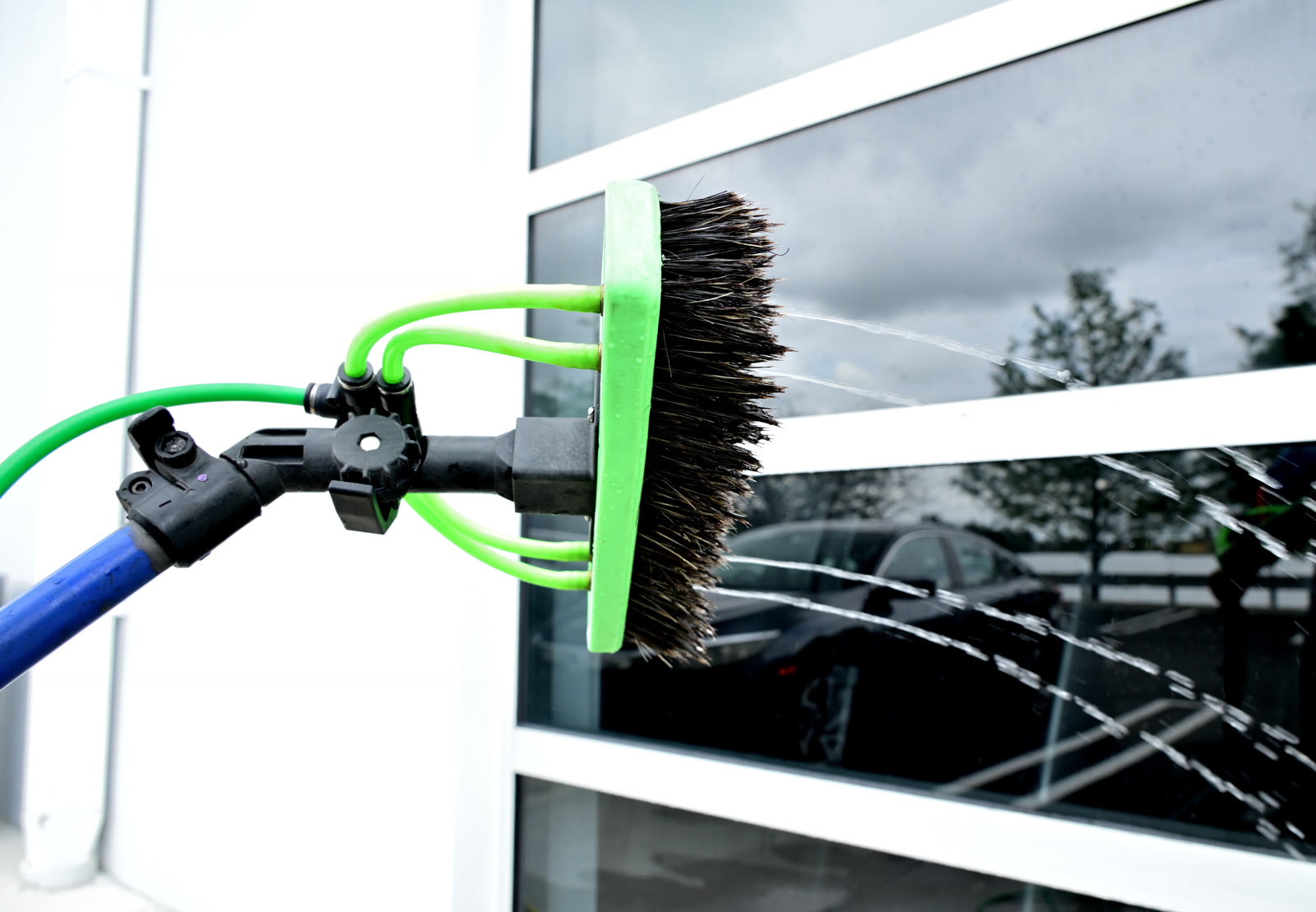 Close-up of a Shiny Windows pure-water-fed pole brush head spraying filtered water across the storefront glass at the Health Choice Network headquarters in Doral, Florida
